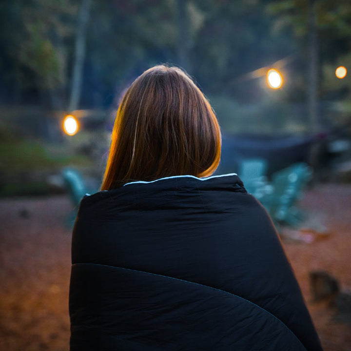 Women using a camping blanket to keep warm outdoors at night.